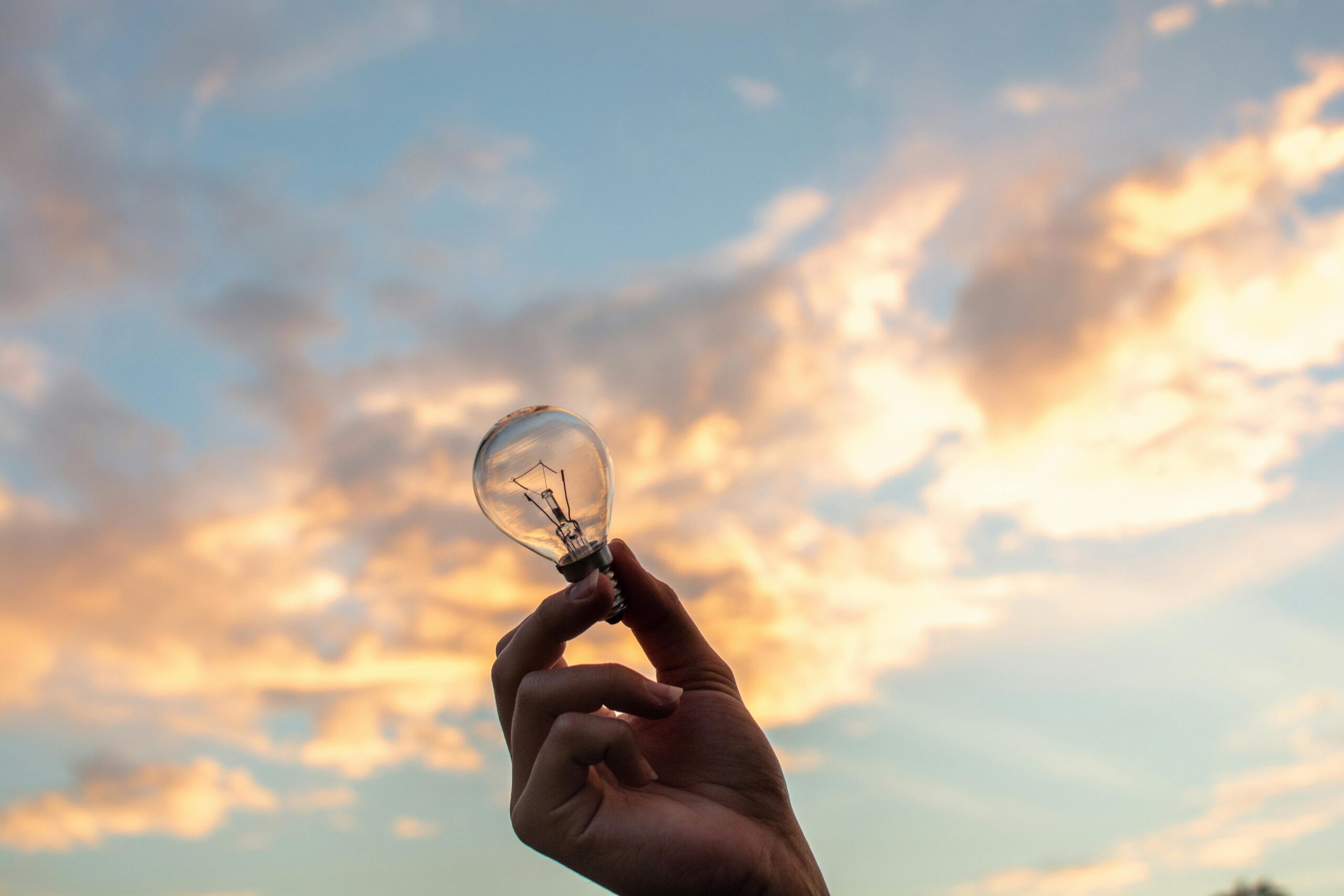 A hand Holding a Lightbulb over Yellow Clouds
