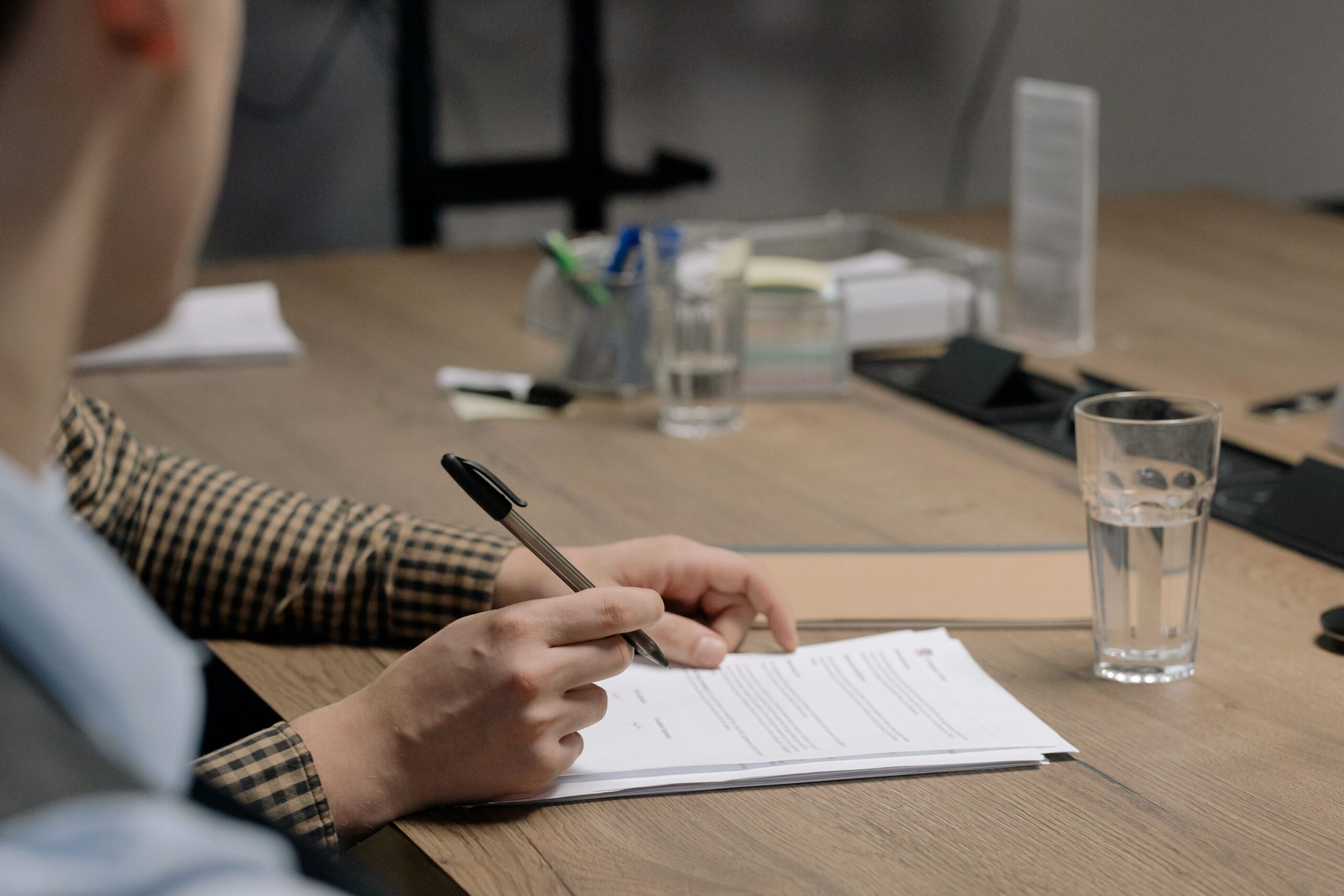 Executor Law - 7 Common Misconceptions About Wills in South Africa A close-up of a person's hands holding a pen over a legal document on a wooden office table, representing the process of drafting wills in south africa.